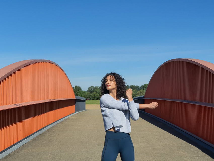 相片由遠攝鏡頭拍攝，相中是一名女士正在灰色閘門和橙色點飾的橋上拉筋，背景是明亮的藍色天空。