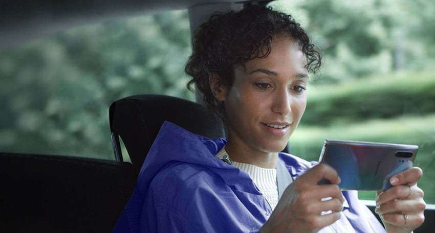 女士正坐在車內，手持橫向的Galaxy Note10+。下載管理的提示正在顯示同時下載三個大型檔案，這全靠兼容快速數據的功能。